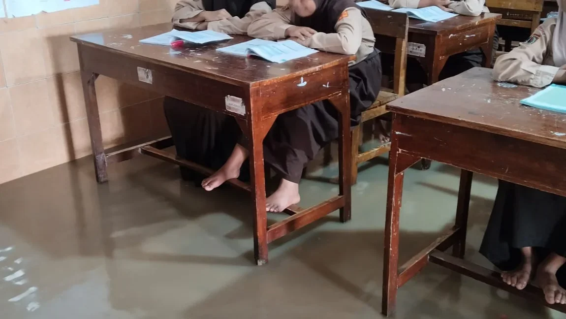 Puluhan murid tetap antusias mengikuti Kegiatan Belajar Mengajar dalam ruang kelas meski kondisi lantai tergenang.