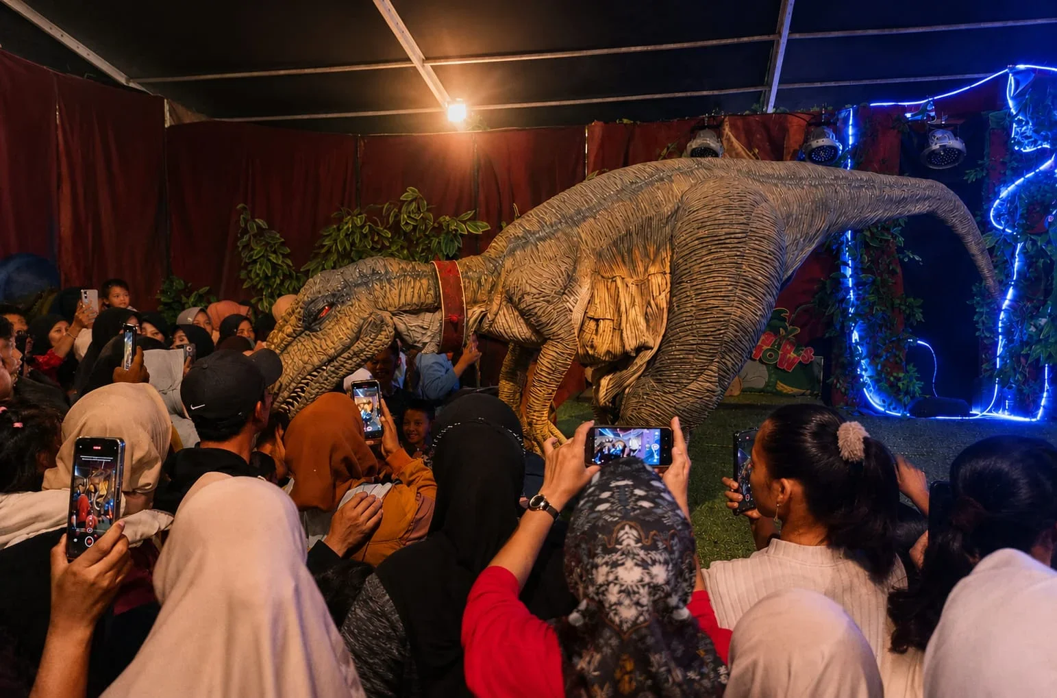 PENGUNJUNG ANTUSIAS – Pengunjung mengabadikan kemunculan dinosaurus dalam pertunjukan Wahana Dinosaurus GBF 2026, di Lapangan Asri, Bumiayu, Kabupaten Brebes.